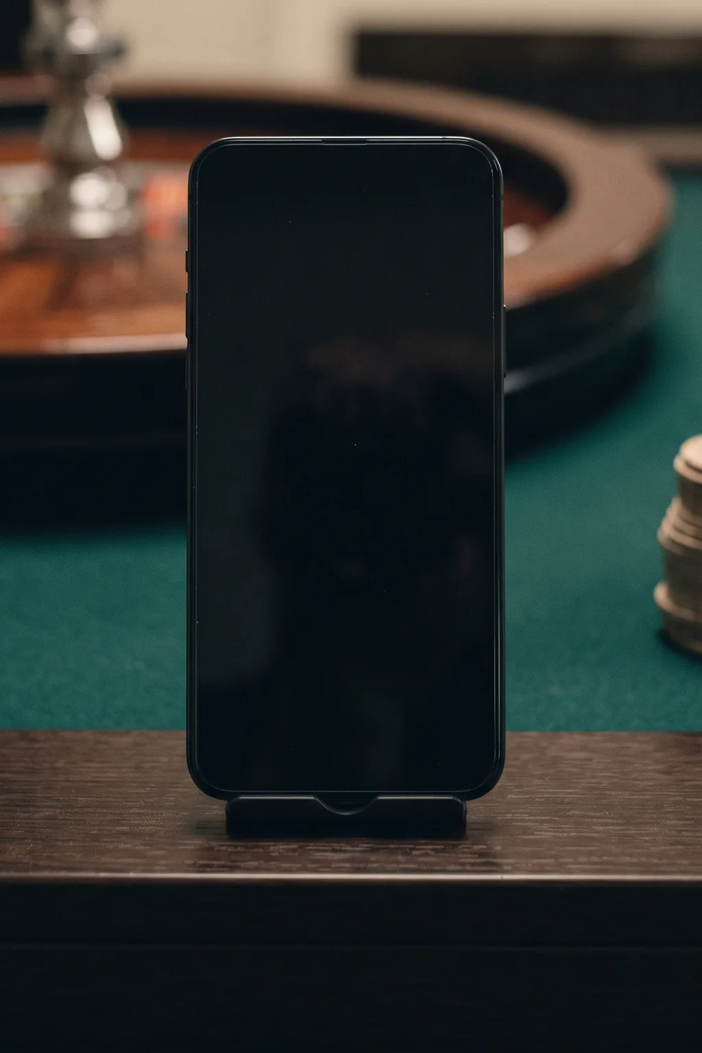 Smartphone on a dark casino table, surrounded by chips and a roulette wheel